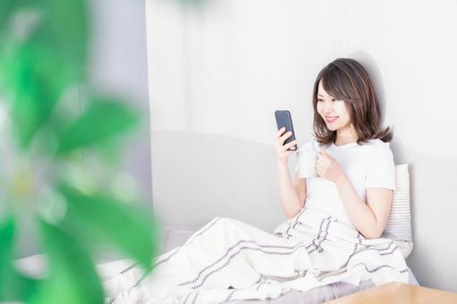 ベッドでスマホを使う若い女性 ベッドでスマホを使う若い女性 くつろぐ,コーヒー,ライフスタイルの写真素材