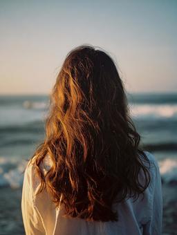 夕日に染まる海を見つめる女性の後ろ姿 夕日に染まる海を見つめる女性の後ろ姿の写真