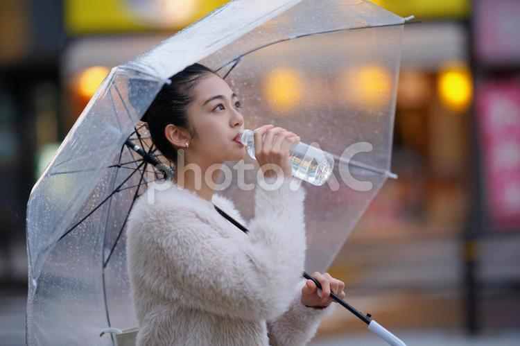 透明な傘を差してペットボトルの水を飲む女性 雨,日本人,アジア人の写真素材