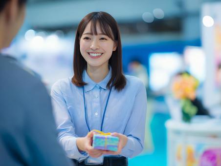 来場者にプレゼントを渡す女性スタッフ 来場者にプレゼントを渡す女性スタッフの写真