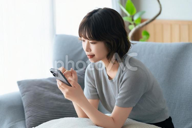 ソファに座ってスマホを使う女性 女性,スマホ,スマートフォンの写真素材
