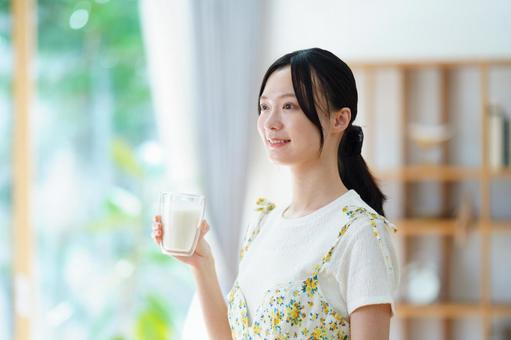 右手で牛乳のコップを持ち微笑む女性の写真