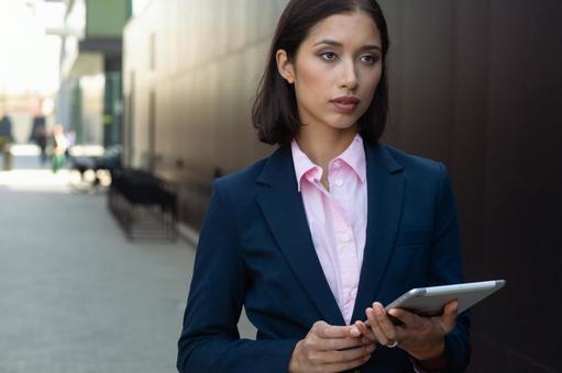 街なかでタブレットを持って立っているスーツの女性 ビジネスウーマン,ビジネス,女性の写真素材