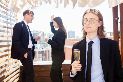 立ち話中の男女の前でグラスを持ち立つ長髪男性の写真