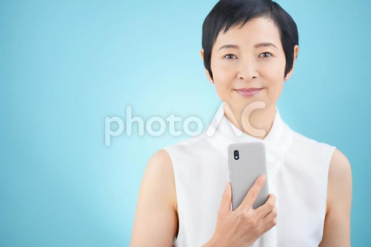 スマートフォンを持っているショートカットの女性（水色背景） 女性,日本人,50代の写真素材