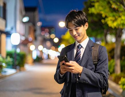 笑顔でスマホを操作する男子高校生 笑顔でスマホを操作する男子高校生の写真