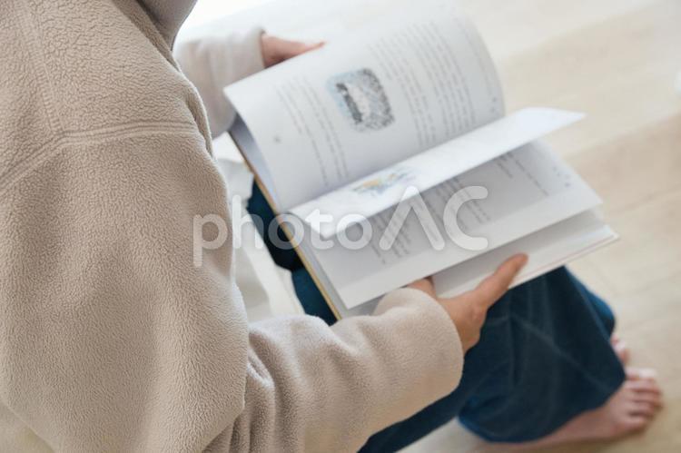 自宅で腰掛けて英文の本を読んでいる女性 本,読書,手元の写真素材