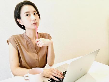 A woman thinking with a pen in front of a computer, JPG