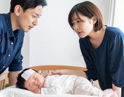 熱を出す赤ちゃんを心配そうに見守る夫婦の写真