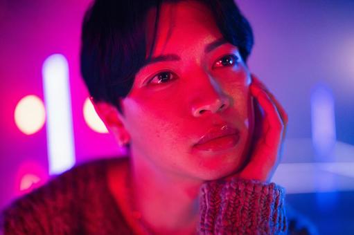 ライトでピンクの頬杖をする男性の顔のアップ ライトでピンクの頬杖をする男性の顔のアップの写真