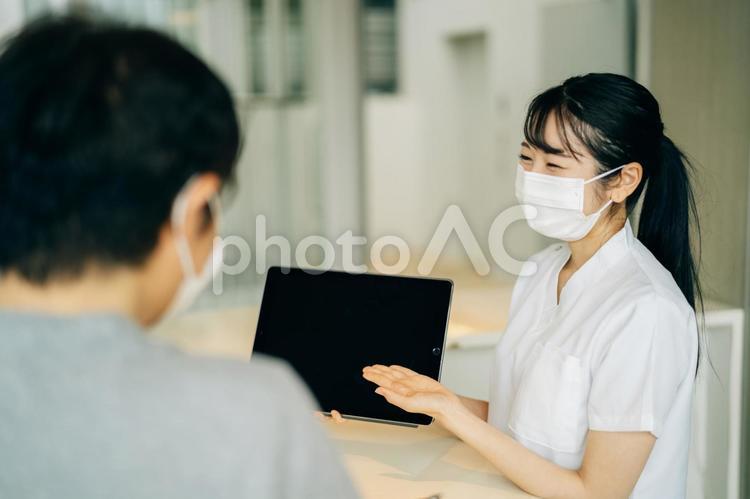 病院の受付にいる女性（マスク・患者・タブレットPC） 医療事務,電子カルテ,タブレットpcの写真素材