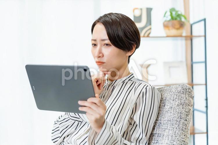 ソファに座りタブレットを見る女性 スマホ,ビジネス,メッセージの写真素材