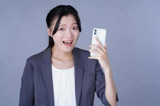 スマホを見て呆れたスーツを着た女性の写真