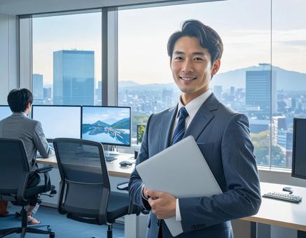オフィスでPCを持って微笑む男性社員 オフィスでPCを持って微笑む男性社員の写真