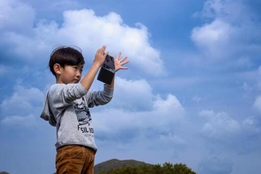 ＜素材＞スマホで春の青空を撮影する男の子 子供,スマホ,空の写真素材