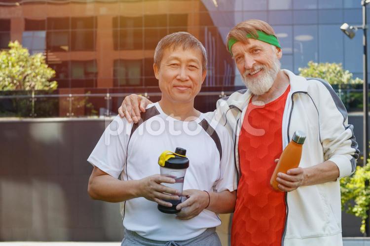 スポーツウェアを着て肩を組んで立つカメラ目線の2人のシニア男性 シニア,スポーツ,男性の写真素材
