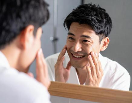 鏡の前で肌の調子をチェックする男性の写真