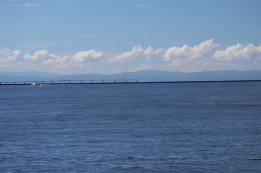 青い海面の海と船と橋と霞む山と雲と青空の写真