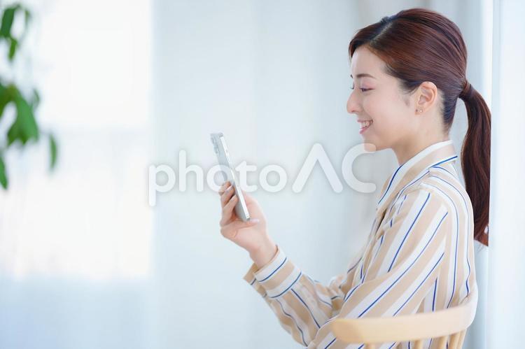 椅子に座ってスマートフォンを見ている女性の横顔 女性,スマートフォン,持つの写真素材