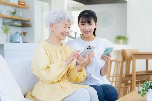 リビングスマホを見てくつろぐ孫と祖母 リビングスマホを見てくつろぐ孫と祖母 家族,シニア,女性の写真素材