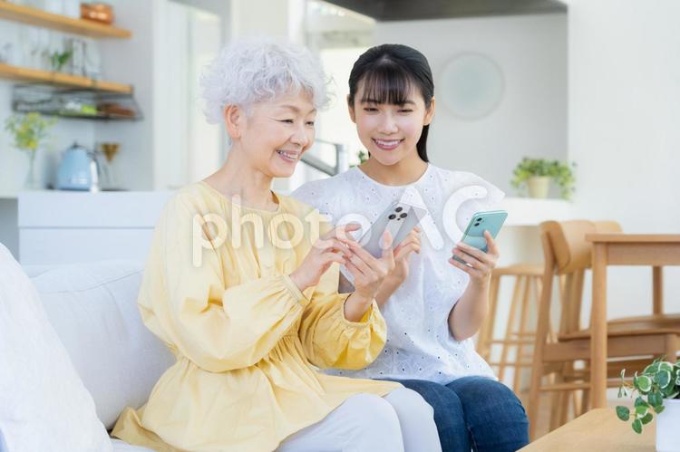 リビングスマホを見てくつろぐ孫と祖母 家族,シニア,女性の写真素材