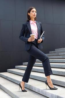 コーヒーとタブレットを持ってオフィスビルの外の階段を登っているビジネスウーマン ビジネスウーマン,ビジネス,女性の写真素材