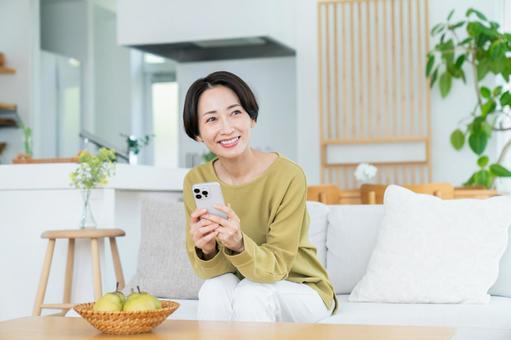 リビングでスマホを使うミドルの女性 リビングでスマホを使うミドルの女性の写真