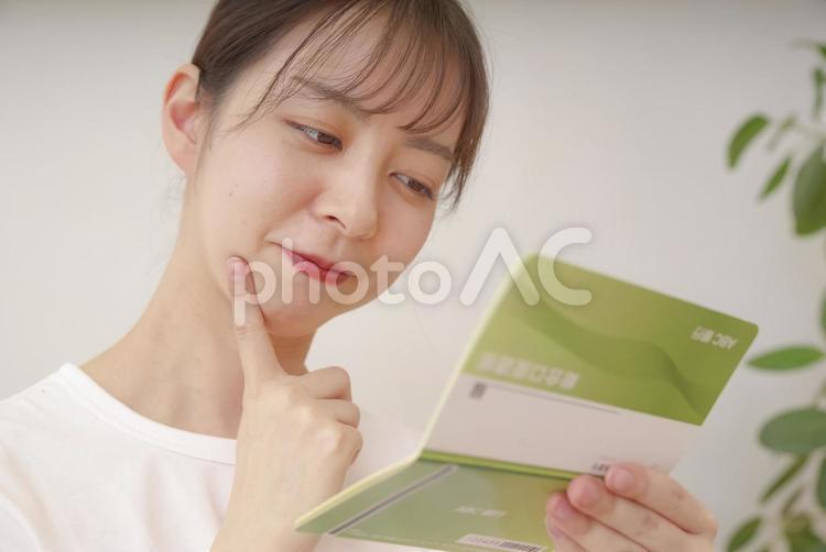 通帳を見て複雑な表情をする女性 女性,悩む,ショックの写真素材