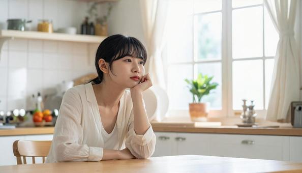 疲れた表情でキッチンに座る若い女性 疲れた表情でキッチンに座る若い女性の写真