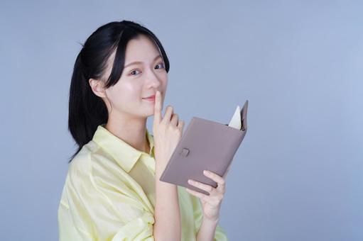内緒ポーズをする黄色い服の女性 女性,手帳,持つの写真素材