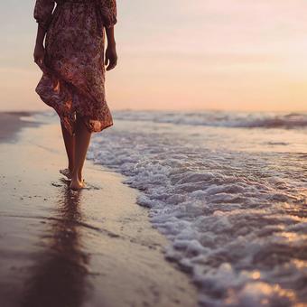 夕日に輝くビーチを歩く女性の足元の写真