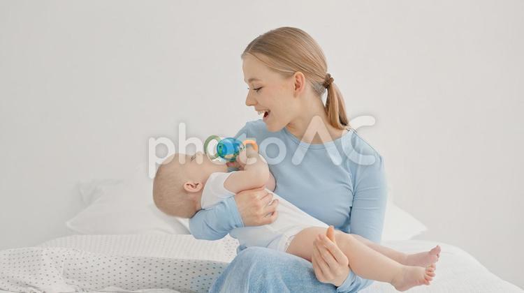 玩具を口に入れようとする赤ちゃんを見る笑顔の女性 親子,抱っこ,見つめるの写真素材