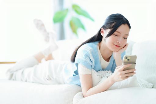 ソファで寛ぎ頬杖をしてスマホを見る女性 女性,スマートフォン,持つの写真素材