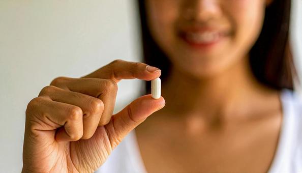 薬一錠を親指と人差し指で持つ女性 薬一錠を親指と人差し指で持つ女性の写真