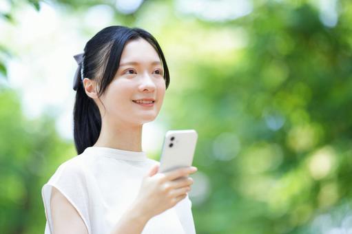 公園で女性がスマホを持つ 女性,笑顔,微笑むの写真素材