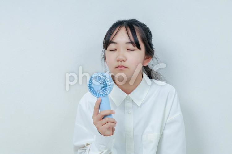 目を閉じてハンディファンで涼む女の子 女性,小学生,少女の写真素材