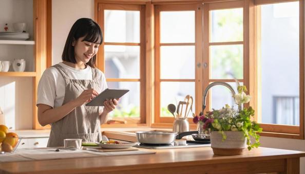 レシピを見ながら料理する日本人の若い女性の写真