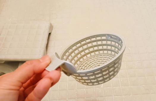 お風呂の排水口のゴミ受けを持つ手の写真