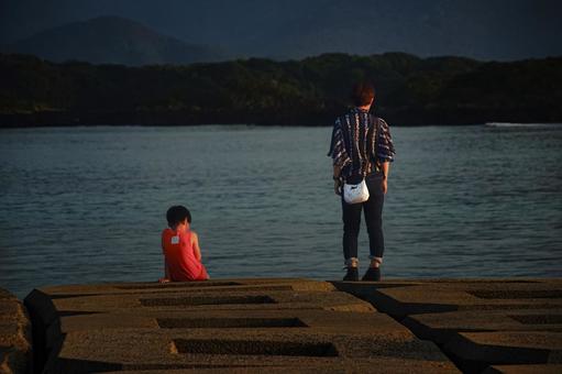 <素材>堤防から夕暮れの海を眺める親子 <素材>堤防から夕暮れの海を眺める親子 家族,親子,女性の写真素材