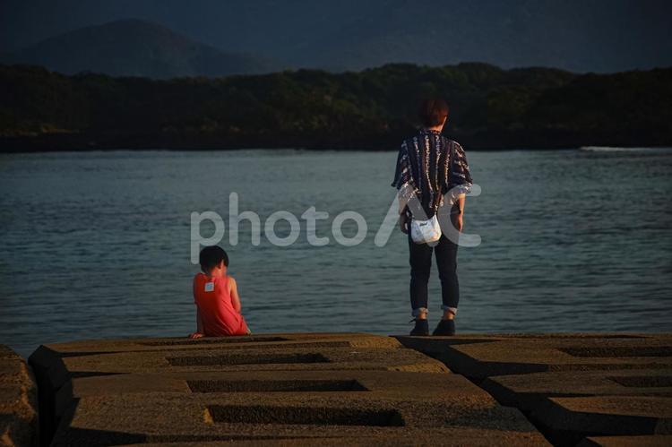 ＜素材＞堤防から夕暮れの海を眺める親子 家族,親子,女性の写真素材