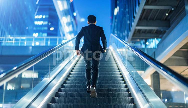 夜のエスカレーターを昇るビジネスマン ビジネスマン,エスカレーター,駆け上がるの写真素材