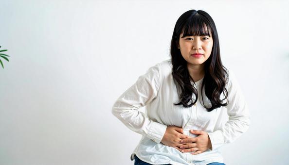 お腹の調子が悪くてお腹をさする若い女性 お腹の調子が悪くてお腹をさする若い女性の写真