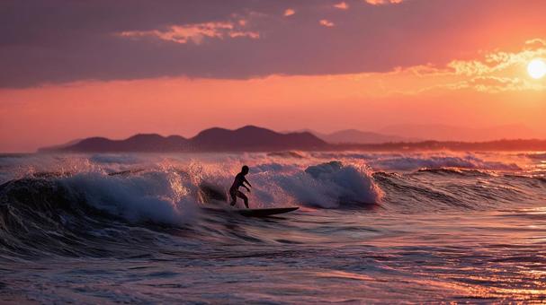 夕暮れの海で最後の波に乗るサーファー女性 夕暮れの海で最後の波に乗るサーファー女性の写真