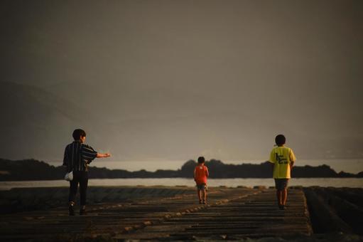 <素材>堤防から夕暮れの海を眺める家族 <素材>堤防から夕暮れの海を眺める家族 家族,女性,子供の写真素材