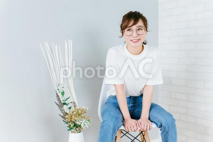 部屋で椅子に座るメガネをかけた日本人女性 メガネ,デニム,眼鏡の写真素材