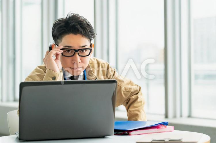 パソコンの前で眼鏡を触る作業着の男性 ビジネス,ビジネスマン,作業員の写真素材