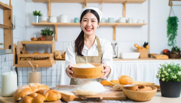 台所で小麦粉をふるいパン作りをする女性 台所で小麦粉をふるいパン作りをする女性の写真