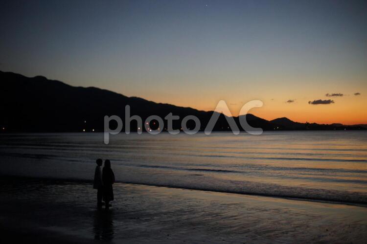 夕焼けの浜辺にたたずむカップル 笑顔,お出かけ,ピアスの写真素材