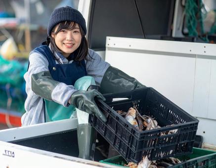 水揚げした魚介類を軽トラに積む漁師の女性の写真