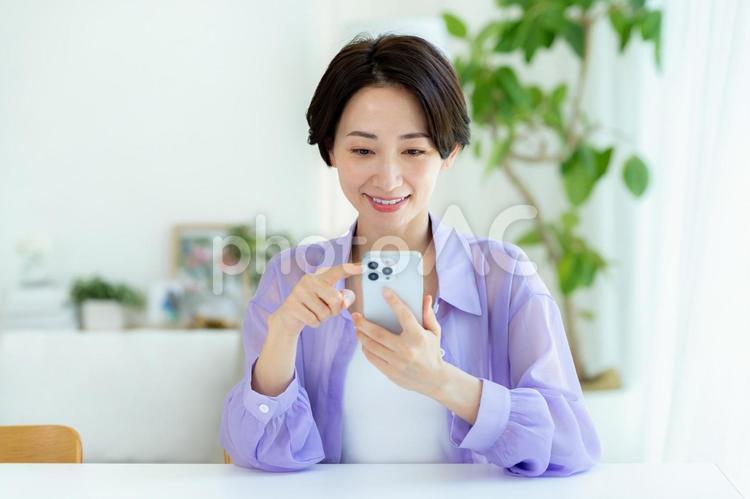 部屋でスマホを操作するミドル女性 スマホ,笑顔,女性の写真素材